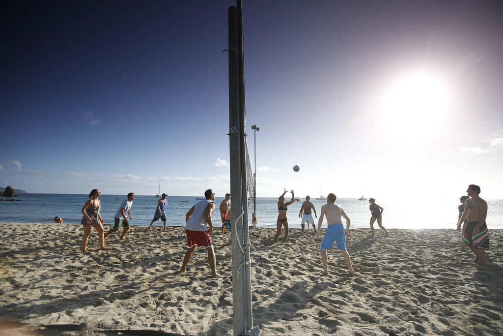 Students playing volleyball in the sun at the beach.