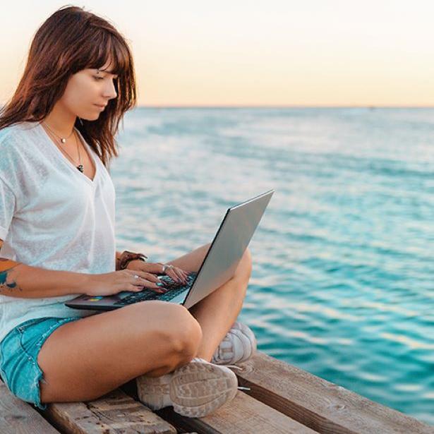 Woman sitting on laptop by the sea