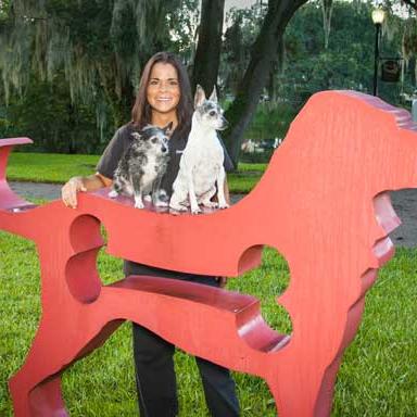 Diane posing with two small dogs on top of a red dog sculpture