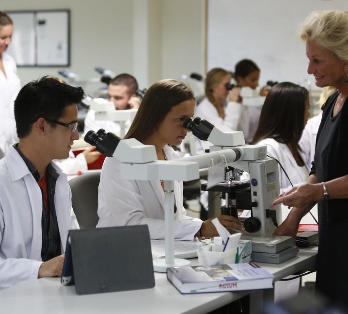 A teacher instructs students in a classroom as they use microscopes.