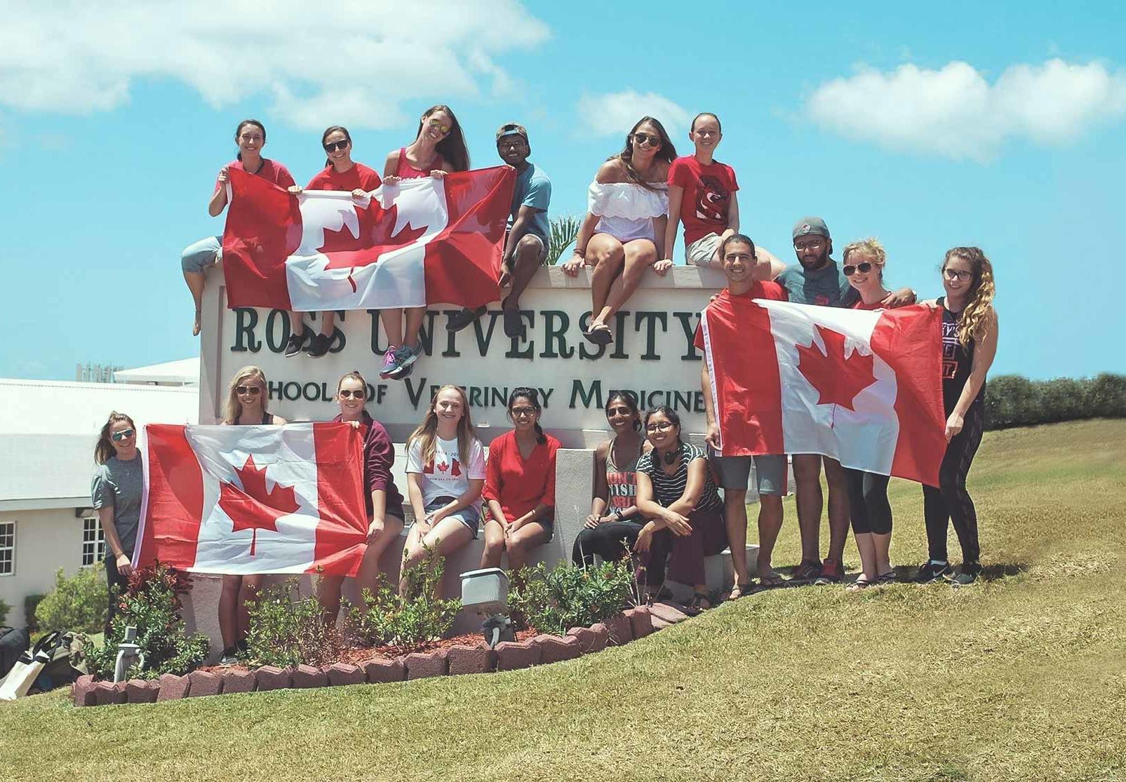 Canadian students holding Canadian flags next to the Ross University School for Veterinary Medicine sign 
