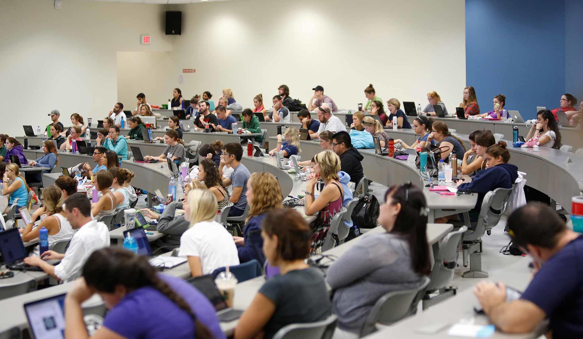 Students listening to a lecture in a large auditorium classroom