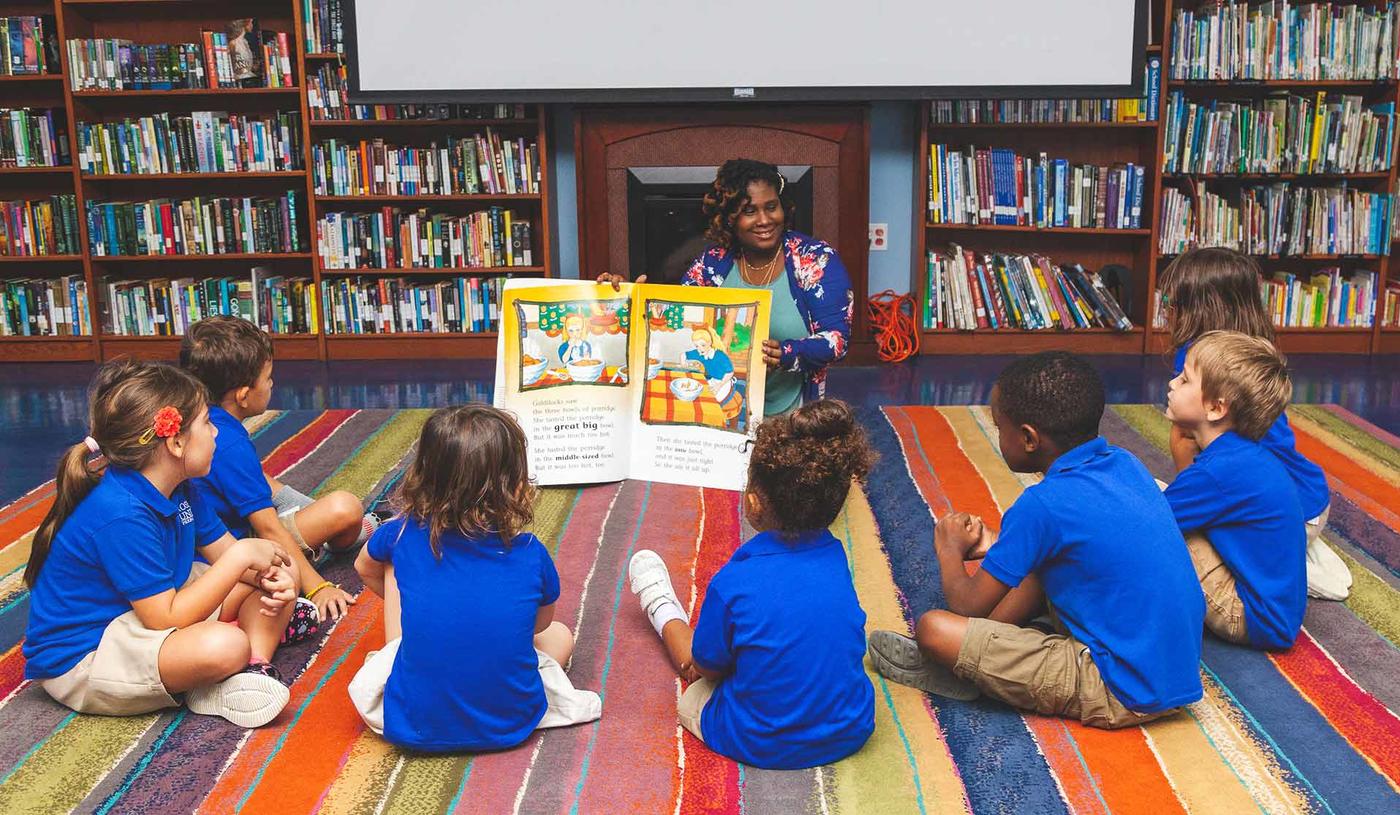 Teacher reading a book to her young students in a library