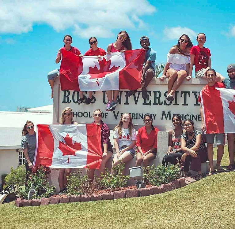 Canadian students holding Canadian flags next to the Ross University School for Veterinary Medicine sign 