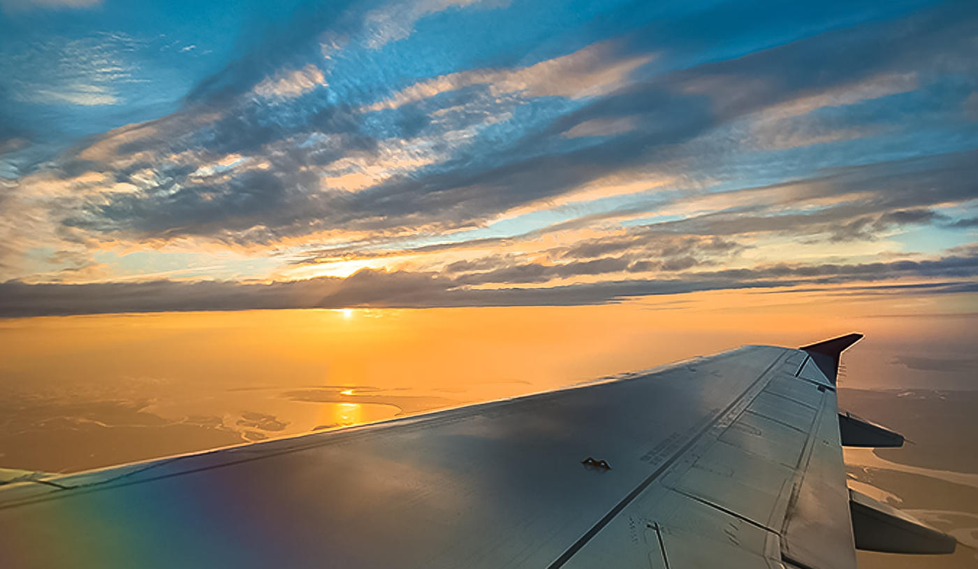 The ocean from above during a sunrise with an airplane wing shown in frame