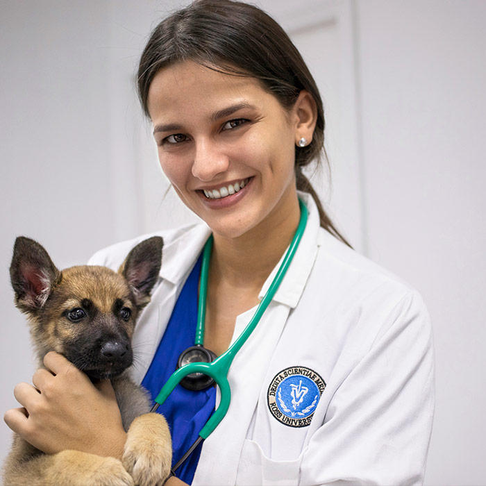 Student in white coat caring for a puppy