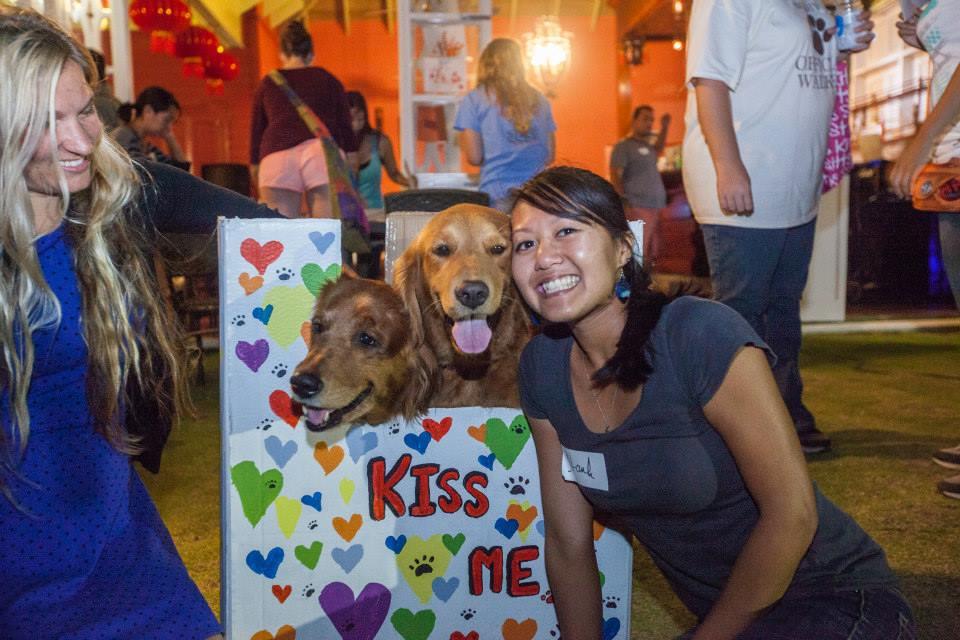 Student posing with two golden retrievers who are behind a "kiss me" booth