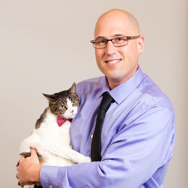 Man posing holding a cat with a bowtie