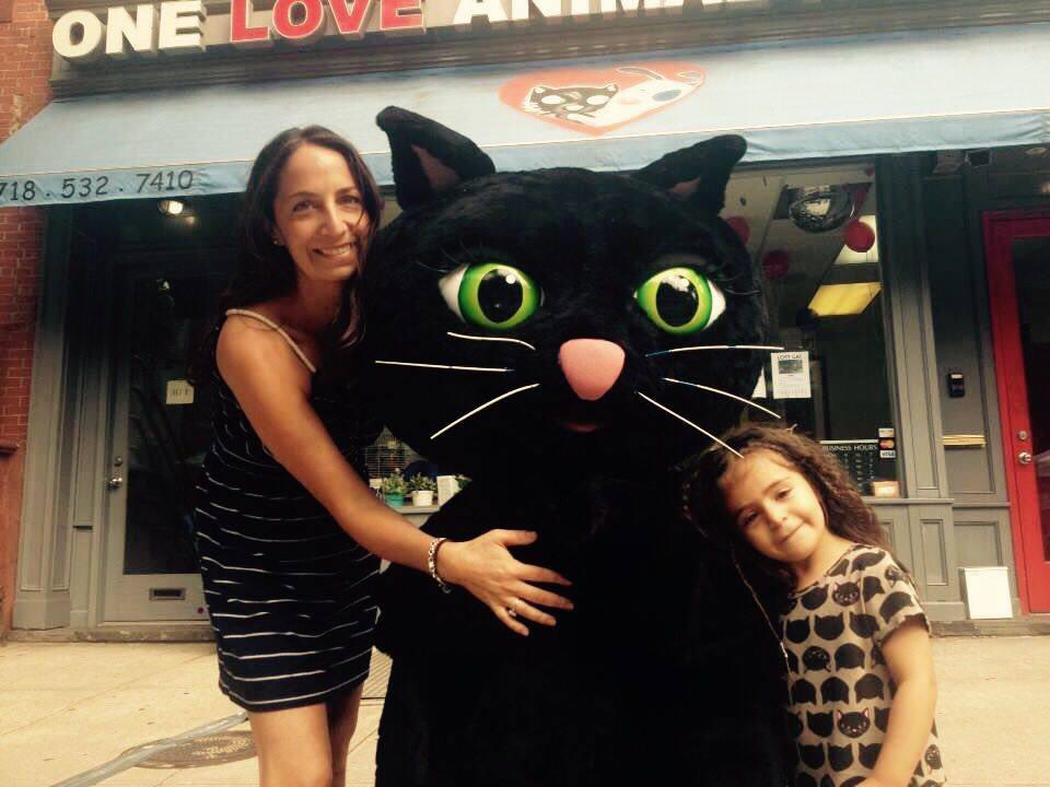 A woman and girl stand on either side of a someone in a life-size cat costume, hugging it.