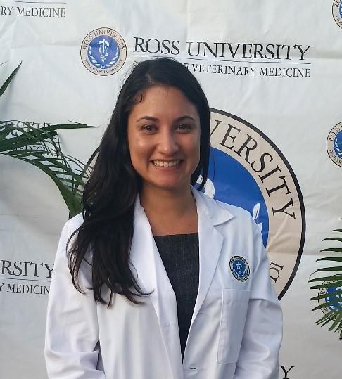 Ross Vet student in a lab coat posing in front of a RUSVM backdrop