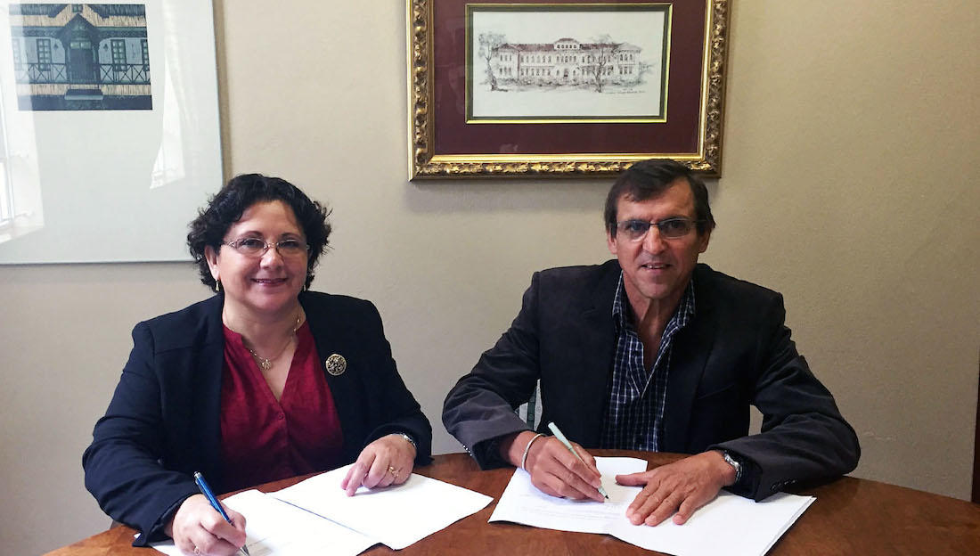 A woman and a man sit at a desk signing papers