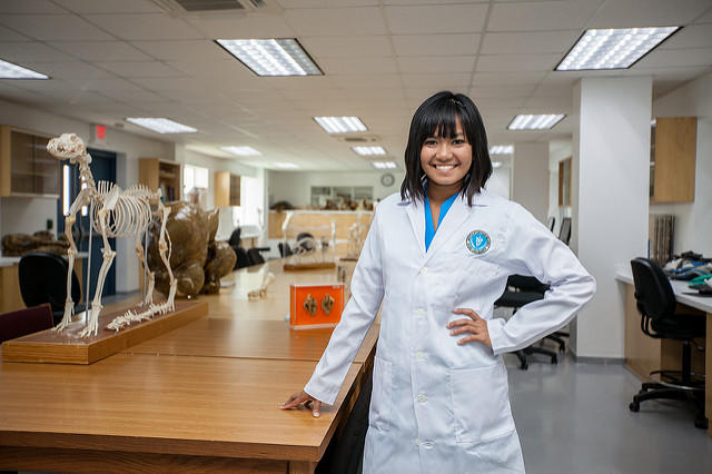 Female veterinary student in lab coat, posing in a classroom.