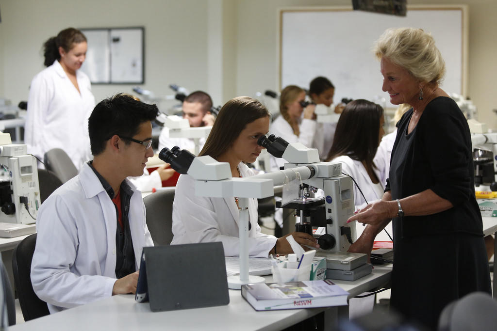 A teacher instructs students in a classroom as they use microscopes.